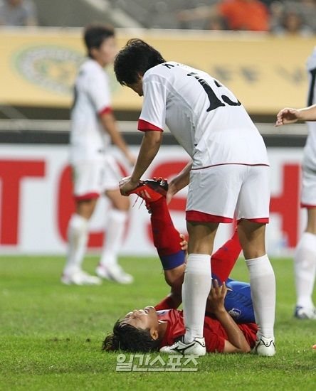 7月21日，“2013东亚杯”女足比赛韩国与朝鲜的比赛在首尔世界杯竞技场举行，图为韩国球员池笑然忽然腿部抽筋倒地，朝鲜球员金南熙（音）走近为她按摩脚部。